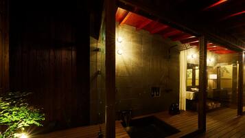 A wooden deck with a glass-enclosed sauna area, stone walls, and a red ceiling.