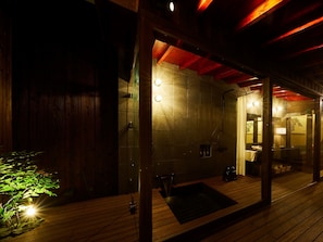 A wooden deck with a glass-enclosed sauna area, stone walls, and a red ceiling.