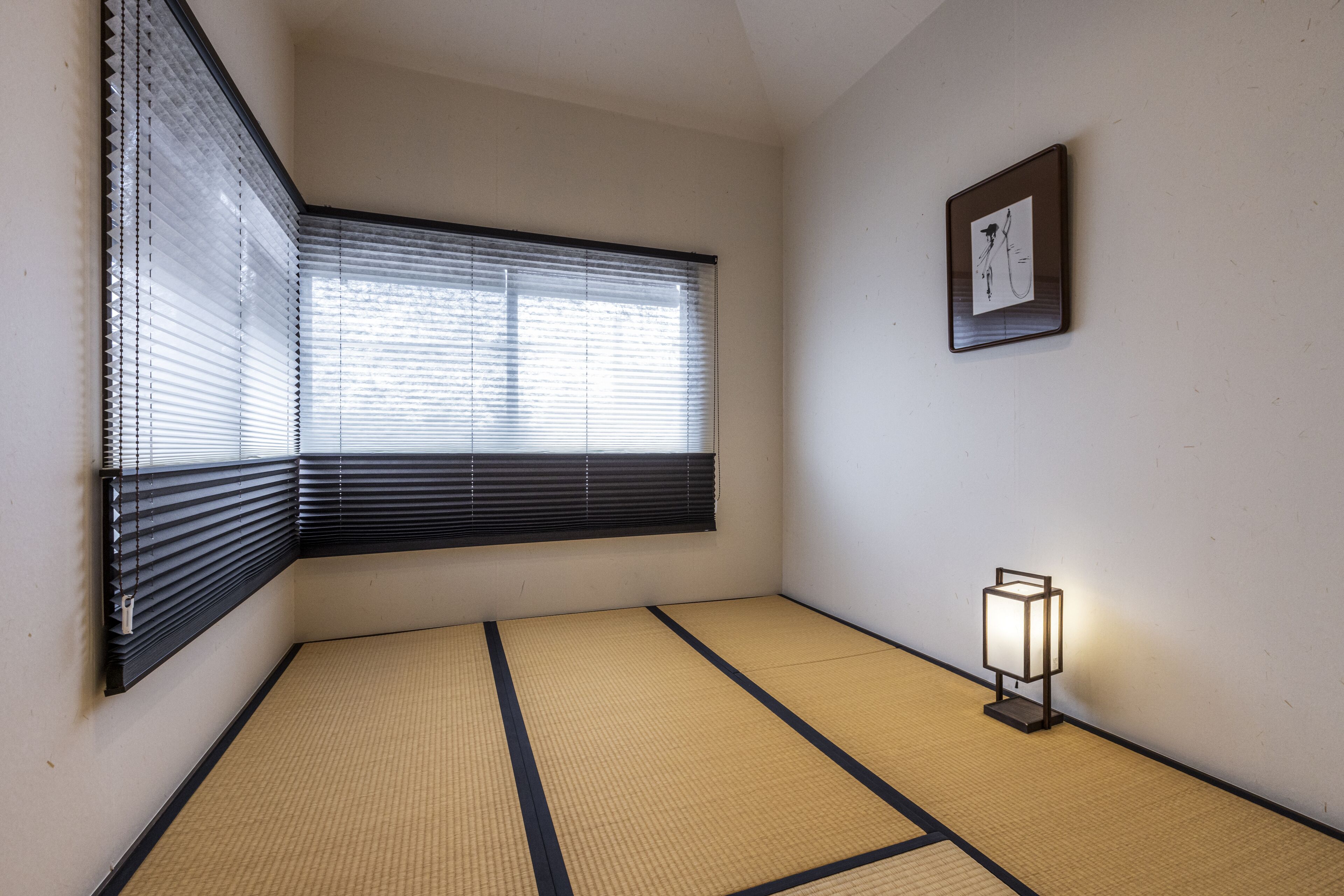 A room with tatami mat flooring, a sliding shoji screen window, a wall-mounted picture frame, and a floor lamp.