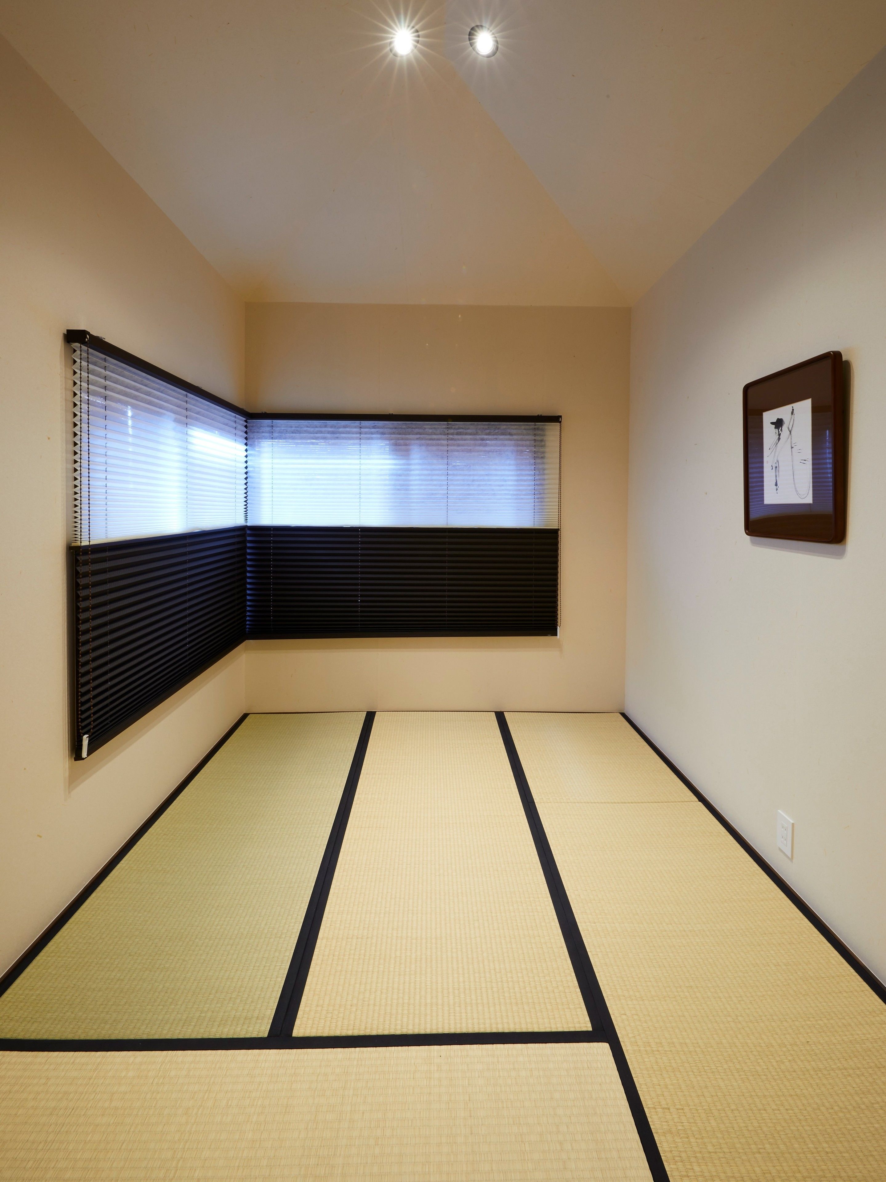 Una habitación con suelo de tatami, una ventana con persianas y un cuadro en la pared.