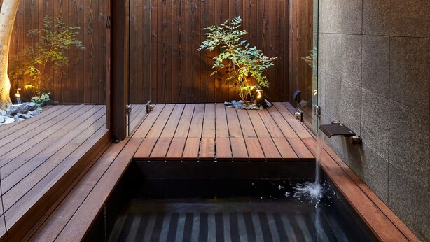 A wooden deck with a small water feature, a wooden fence, and a wall with a light fixture. - Rinn Premium Machiya Townhouse Kyoto Nijo Castle North (Kyoto)