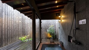 A wooden deck with a small garden, a wooden bench, and a stone wall with a water feature. - Rinn Premium Machiya Townhouse Kyoto Nijo Castle North (Kyoto)