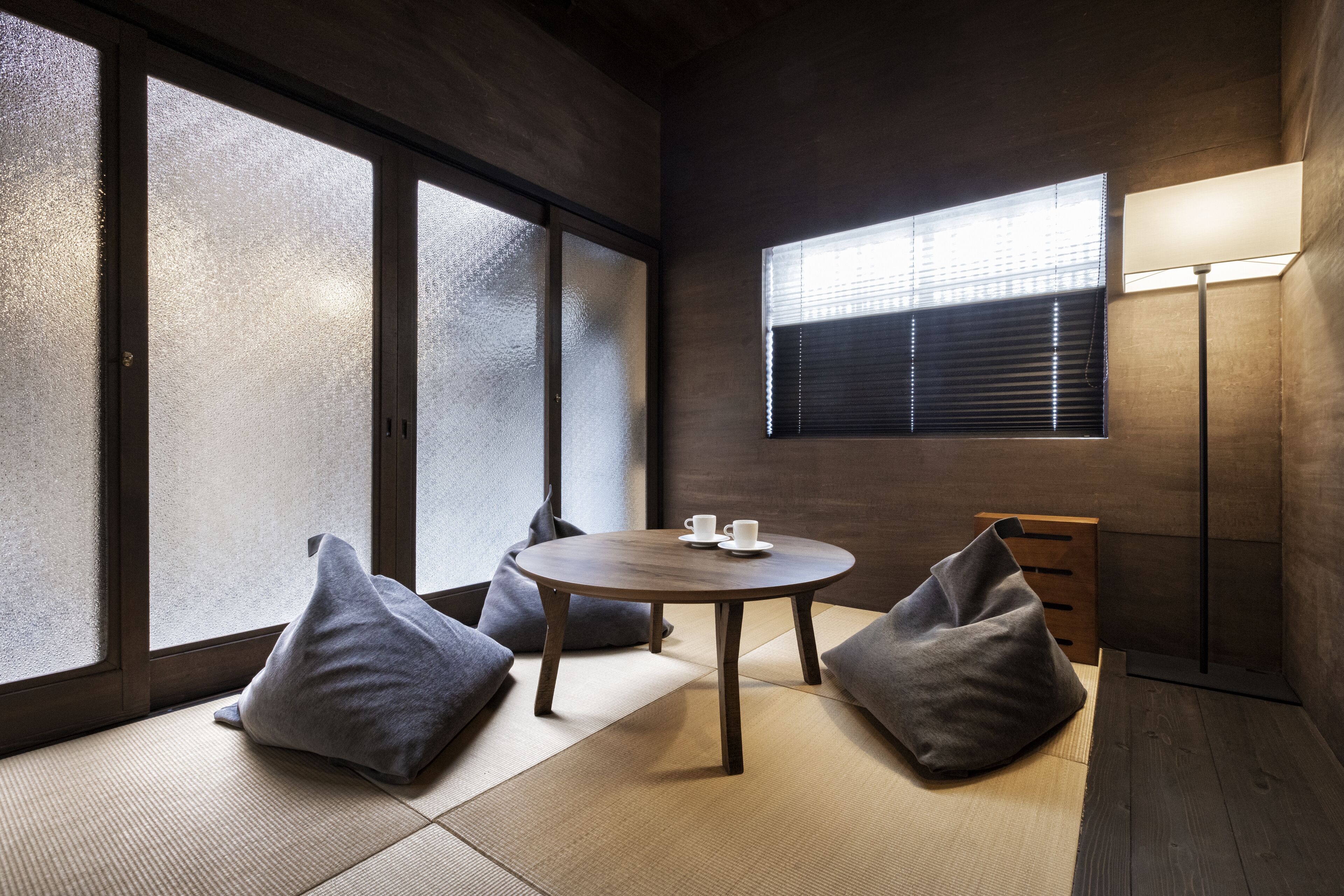 A room with tatami flooring, a round table with two cups, and a lamp.