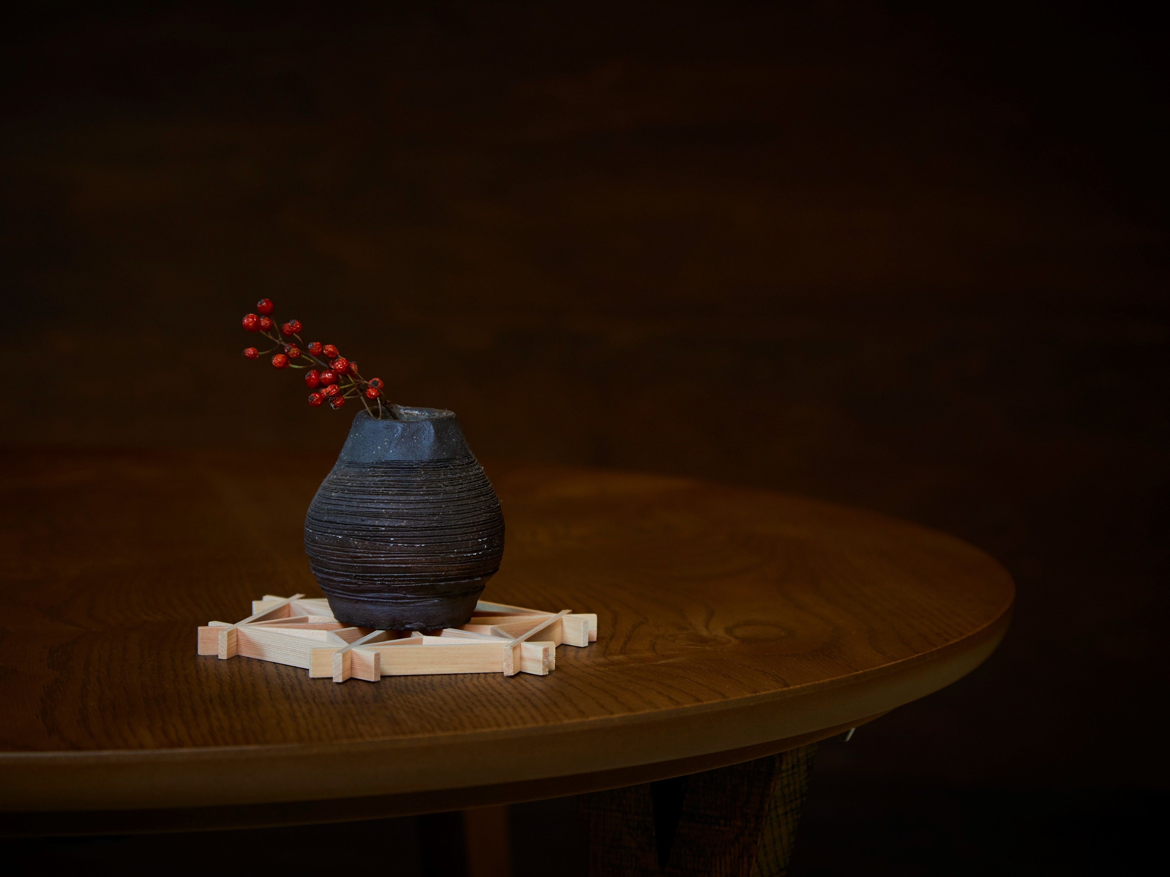 A dark blue vase with red berries on a wooden table.
