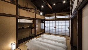 A traditional Japanese room with tatami flooring, a low wooden bed, sliding shoji doors, and a hanging light fixture. - Rinn Premium Machiya Townhouse Kyoto Nijo Castle North (Kyoto)