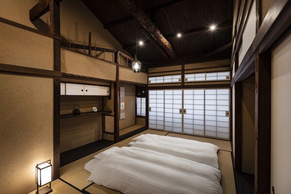 A traditional Japanese room with tatami flooring, a low wooden bed, sliding shoji doors, and a hanging light fixture.