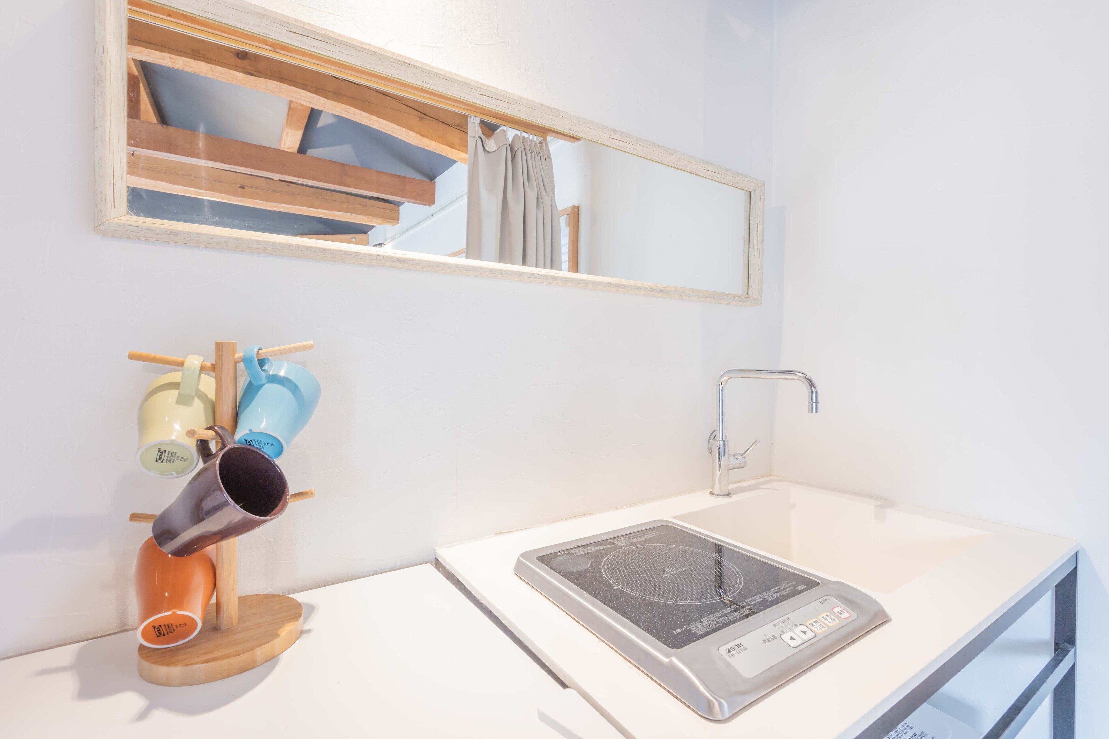 Un baño moderno con un lavabo blanco, una placa de inducción integrada y un soporte de madera para tazas.