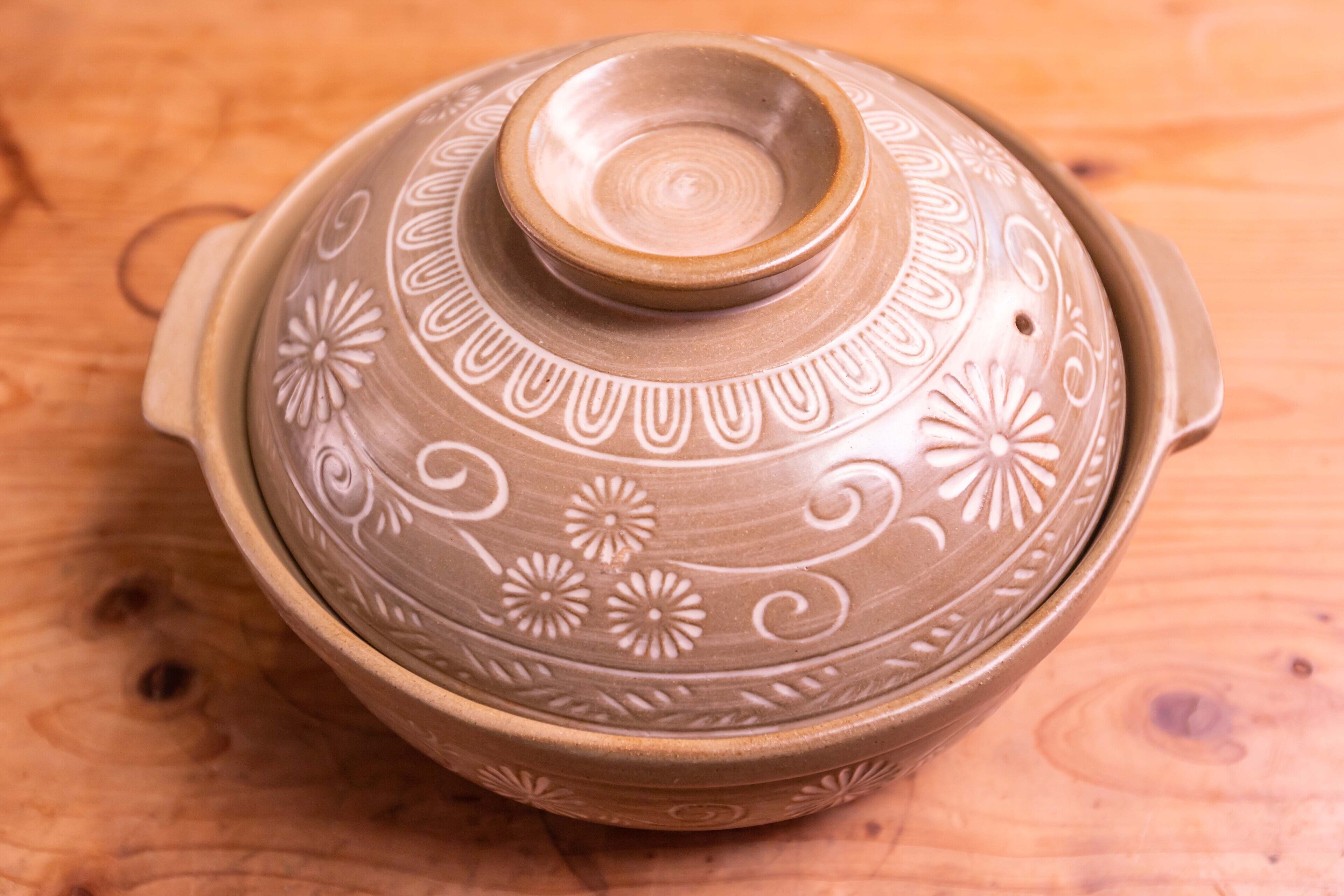 Een keramieken pot met deksel, versierd met bloemen en spiraalmotieven, op een houten ondergrond.