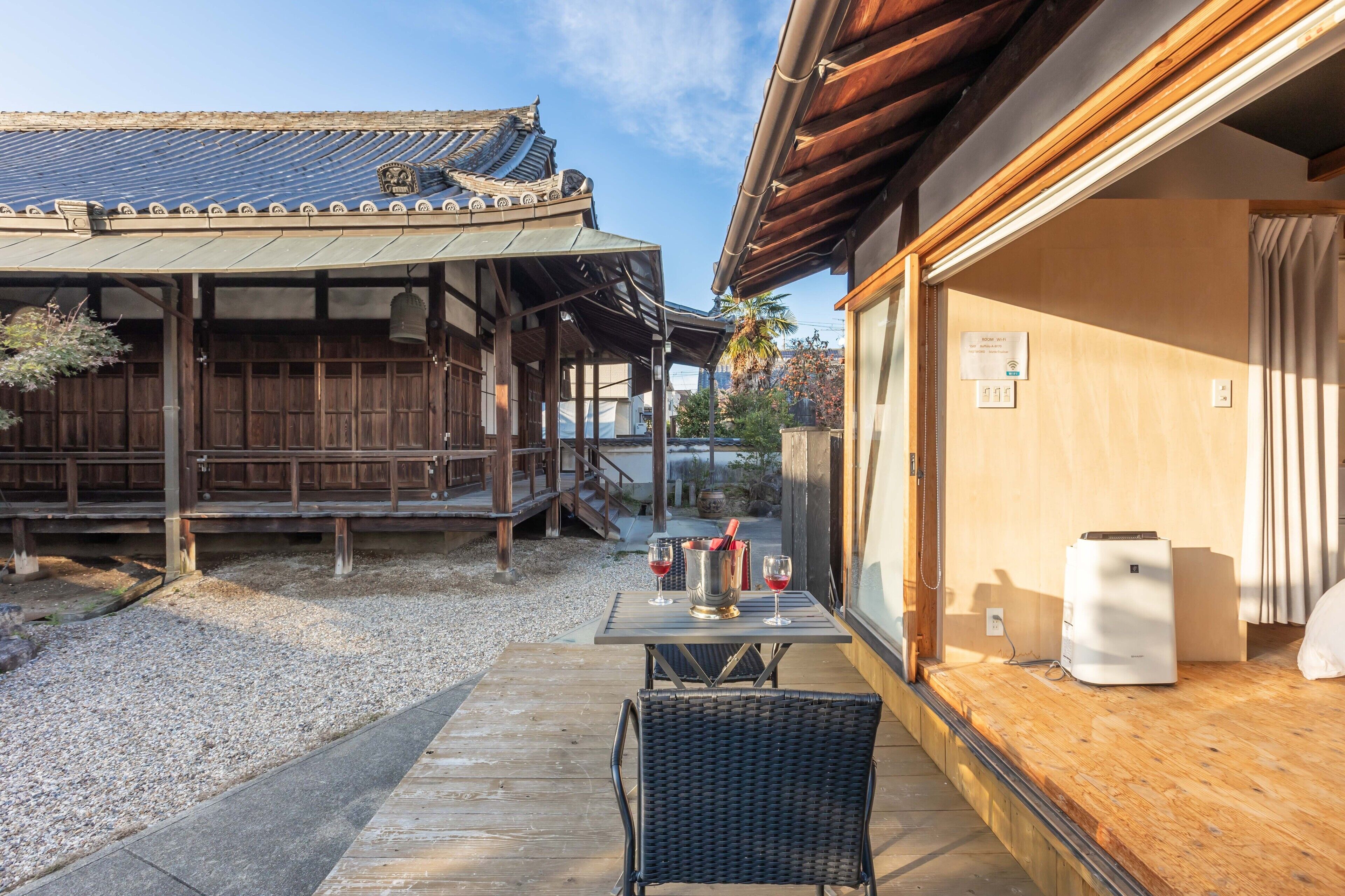 Un bâtiment japonais traditionnel, avec une façade en bois et un espace extérieur aménagé avec des sièges sous une véranda.