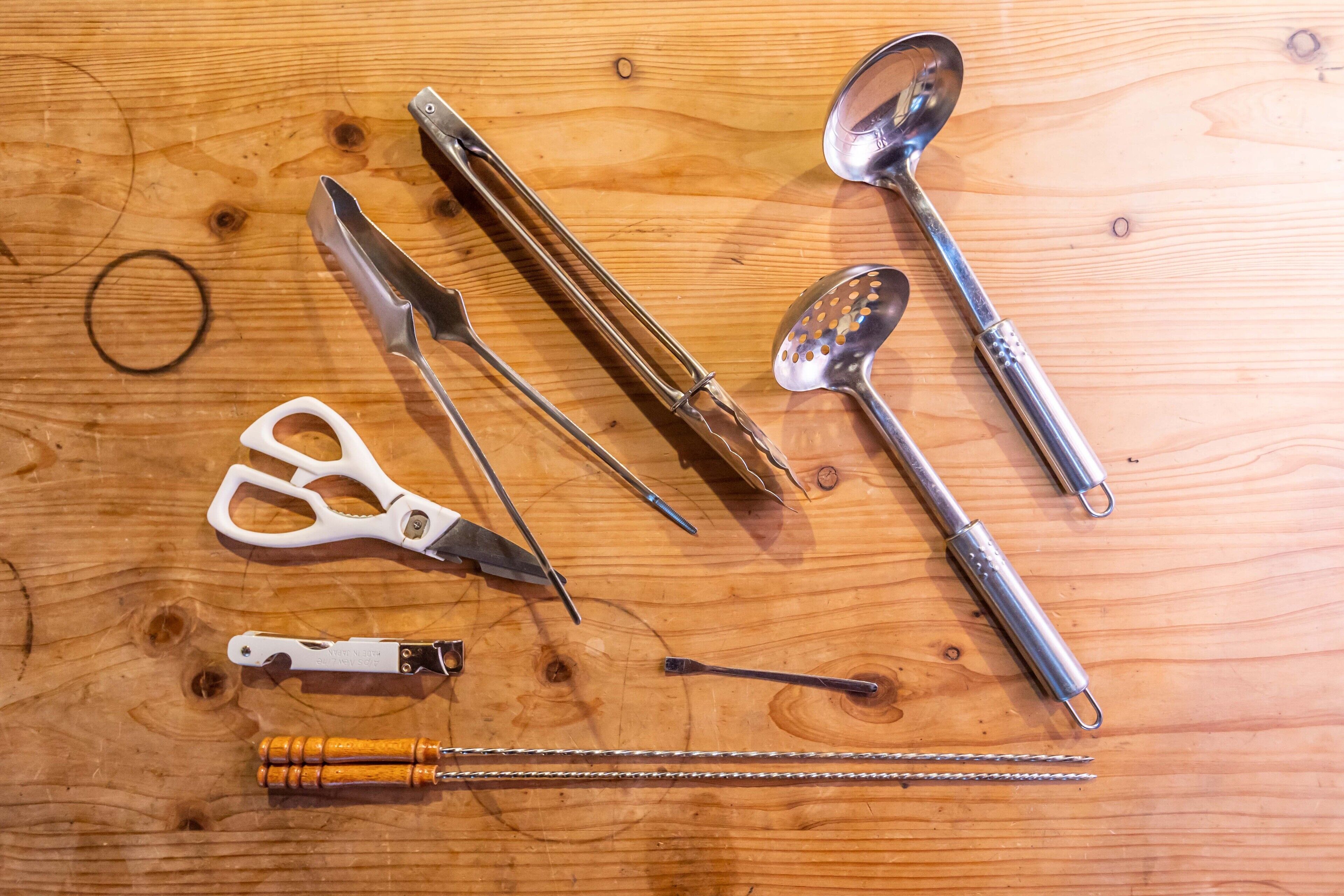 A wooden surface with various metal tools and a white plastic bottle opener.