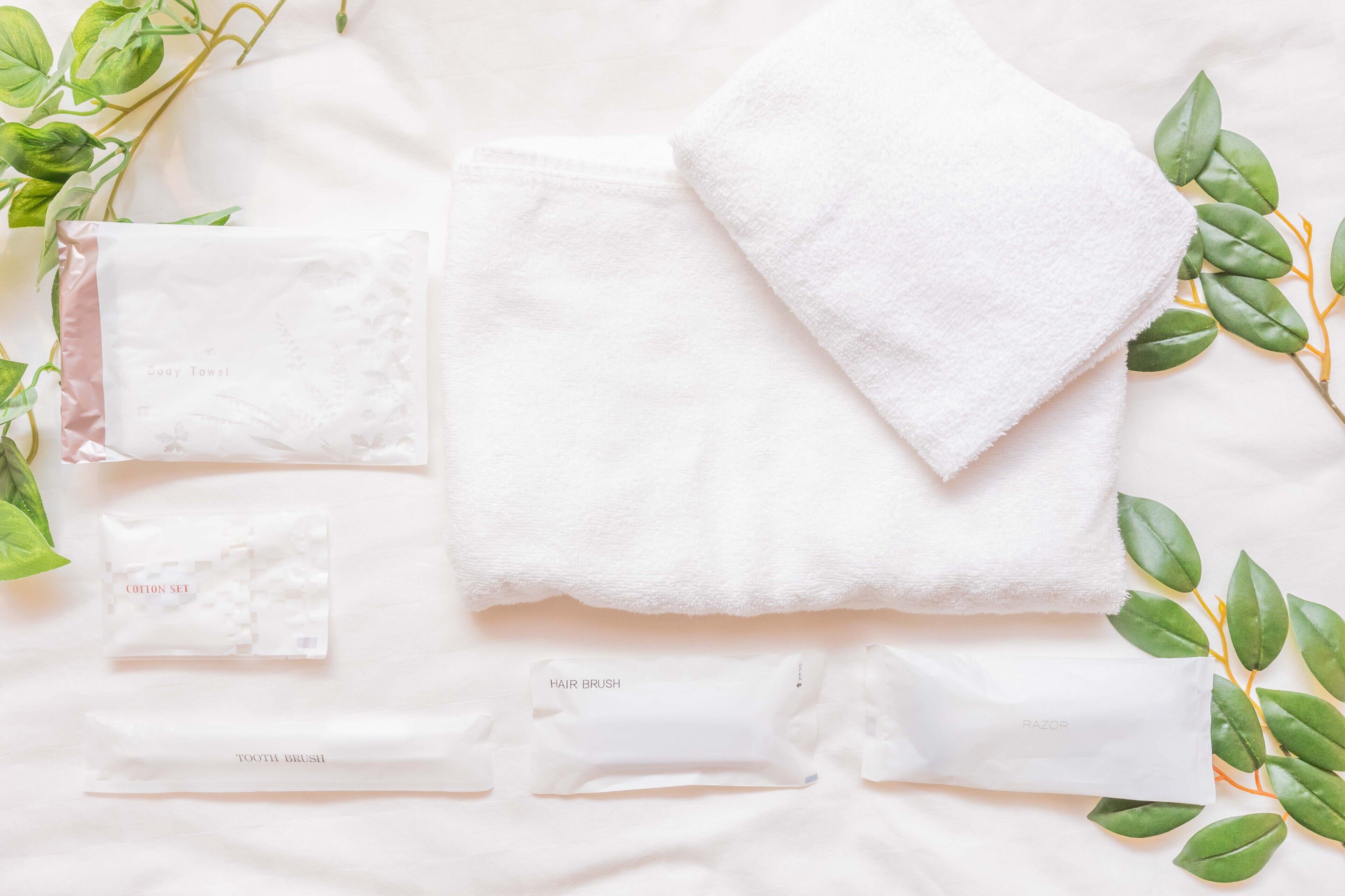 A neatly arranged set of personal care items including a cotton set, hair brush, and razors on a white surface with green leaves.