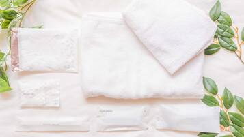 A neatly arranged set of personal care items including a cotton set, hair brush, and razors on a white surface with green leaves.