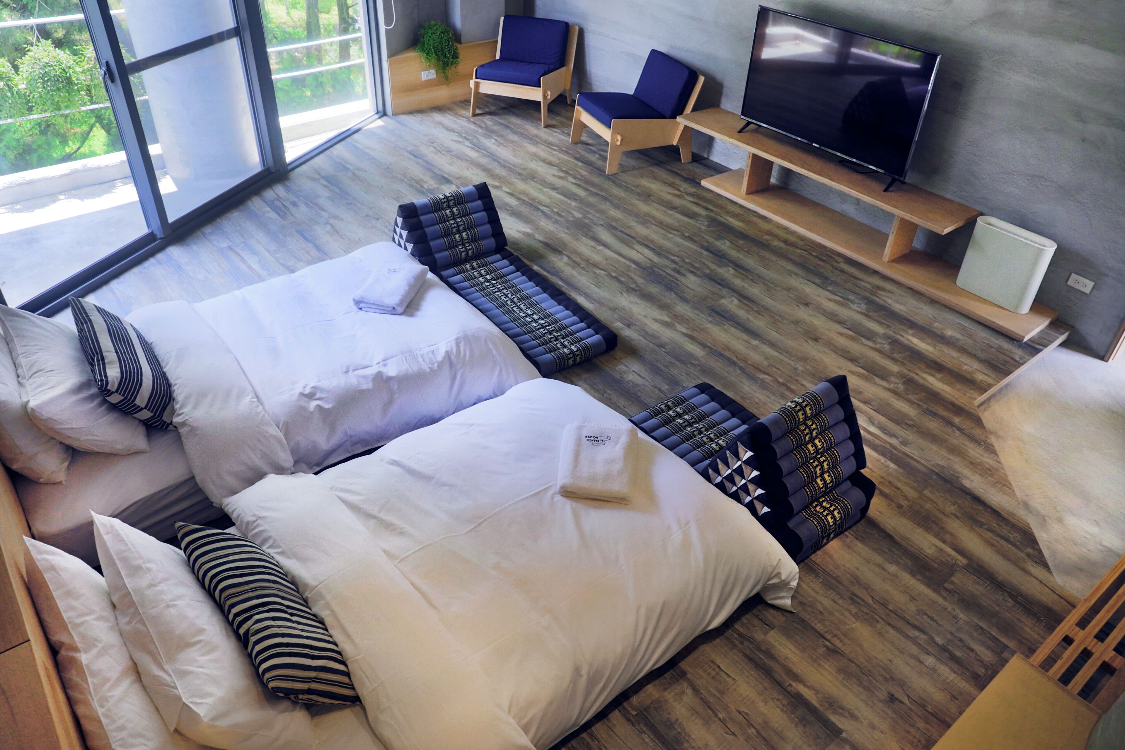 Una habitación de hotel moderna con una cama grande, dos sillones, un televisor y vistas a zonas verdes por las ventanas.