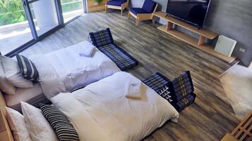 Una habitación de hotel moderna con una cama grande, dos sillones, un televisor y vistas a zonas verdes por las ventanas.