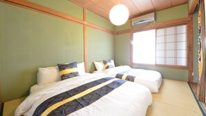 A hotel room with two beds, a large window with shoji screens, tatami flooring, and a ceiling fan. - Private room ROSSO (Osaka)