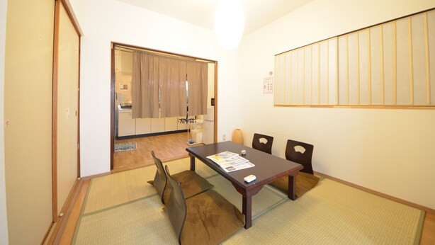 A room with a tatami mat floor, a wooden table with chairs, a sliding door, and a wall-mounted panel. - Private room ROSSO (Osaka)