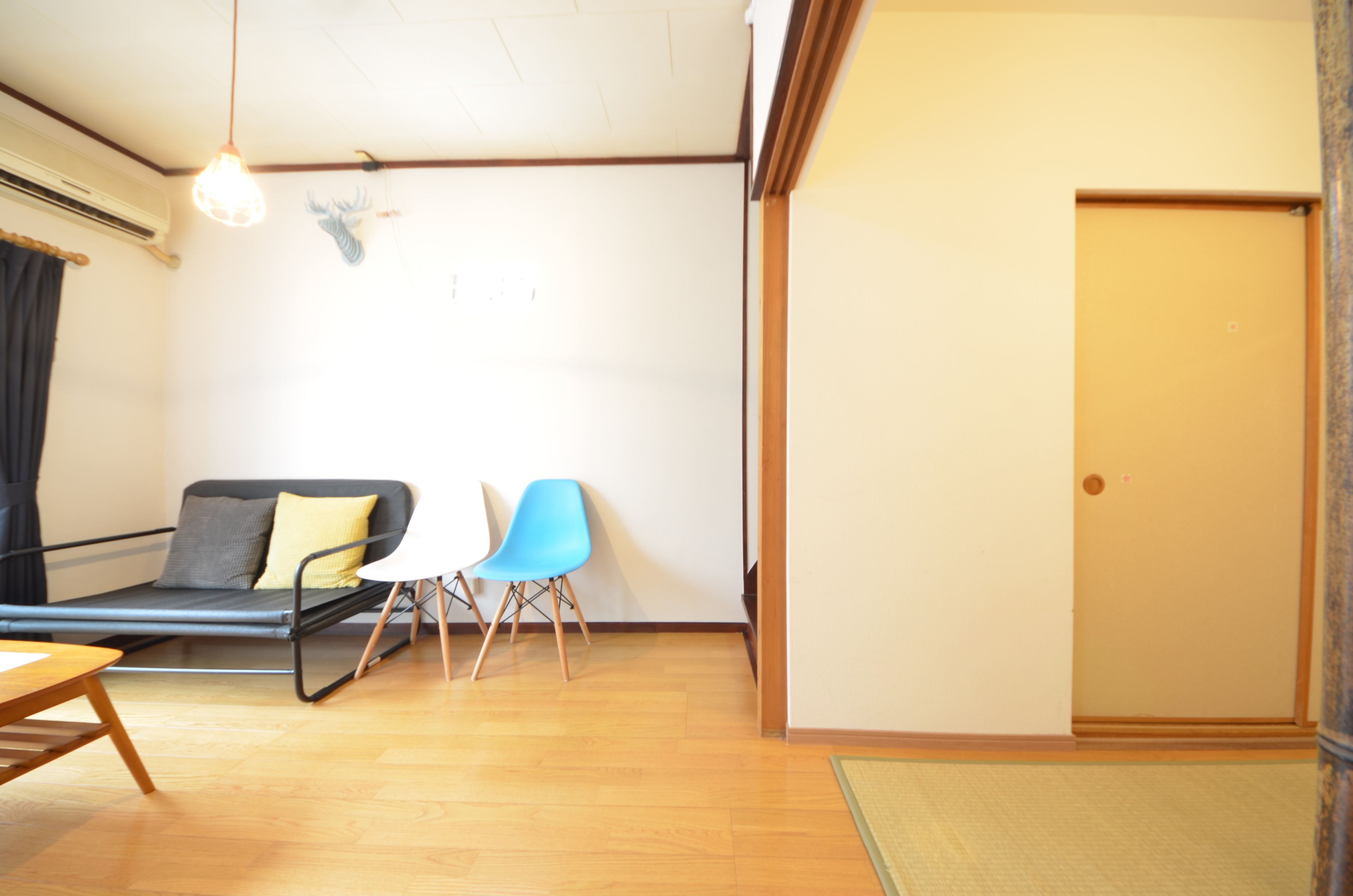 Une pièce comprenant un canapé, deux fauteuils, un plancher en bois, une porte et un luminaire suspendu.