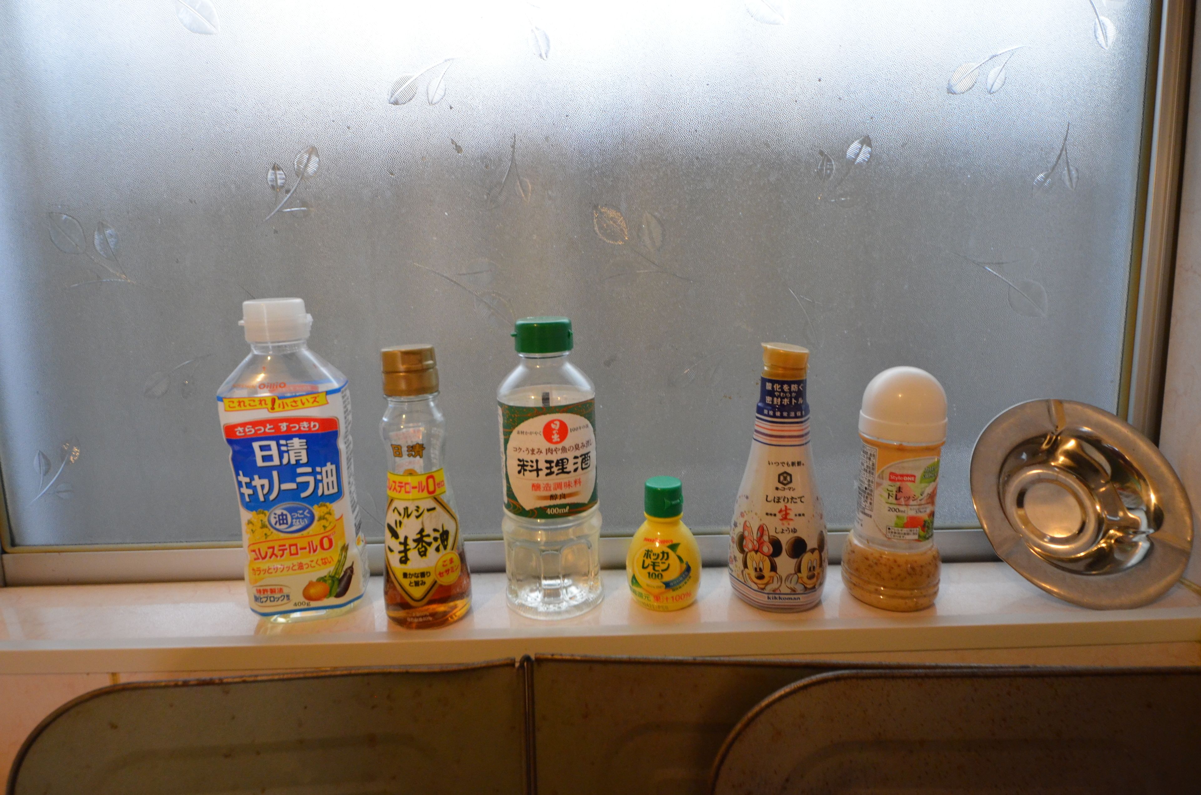 A shelf with various bottles of condiments and a metal dish.