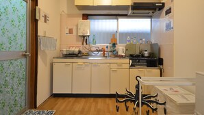 A compact kitchen with white cabinets, a small refrigerator, a stove, and a window with blinds. - Private room ROSSO (Osaka)