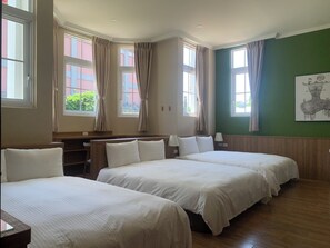 A hotel room with two beds, a desk, and large windows with curtains.