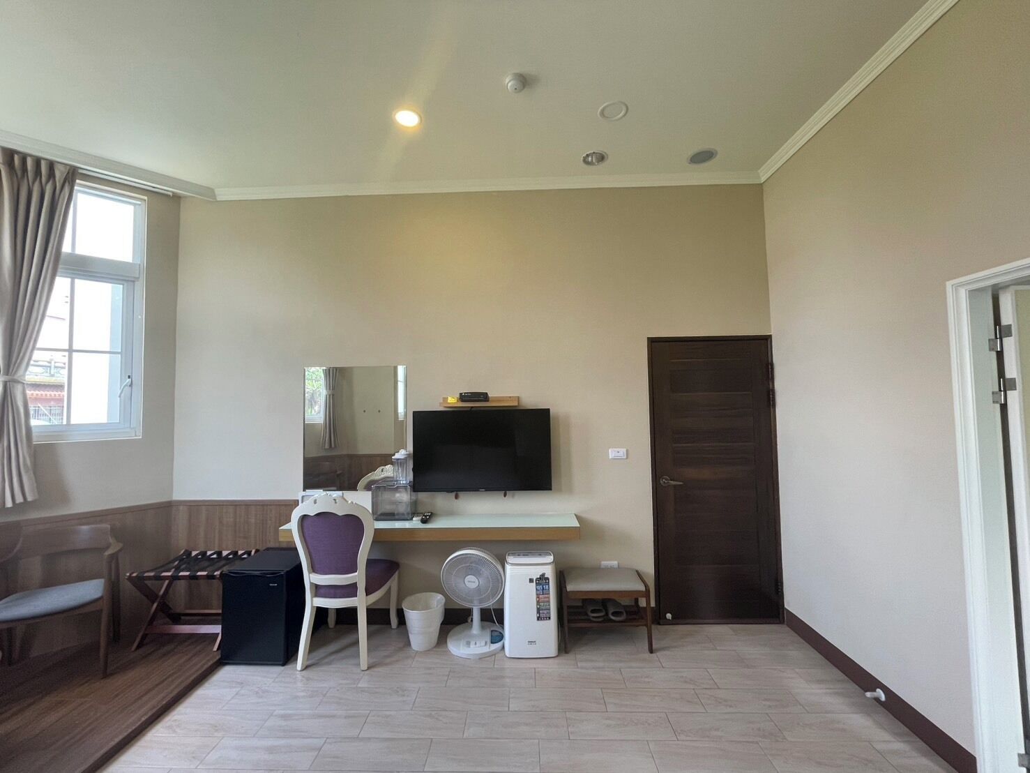 A room with a desk, chair, TV, and a door.