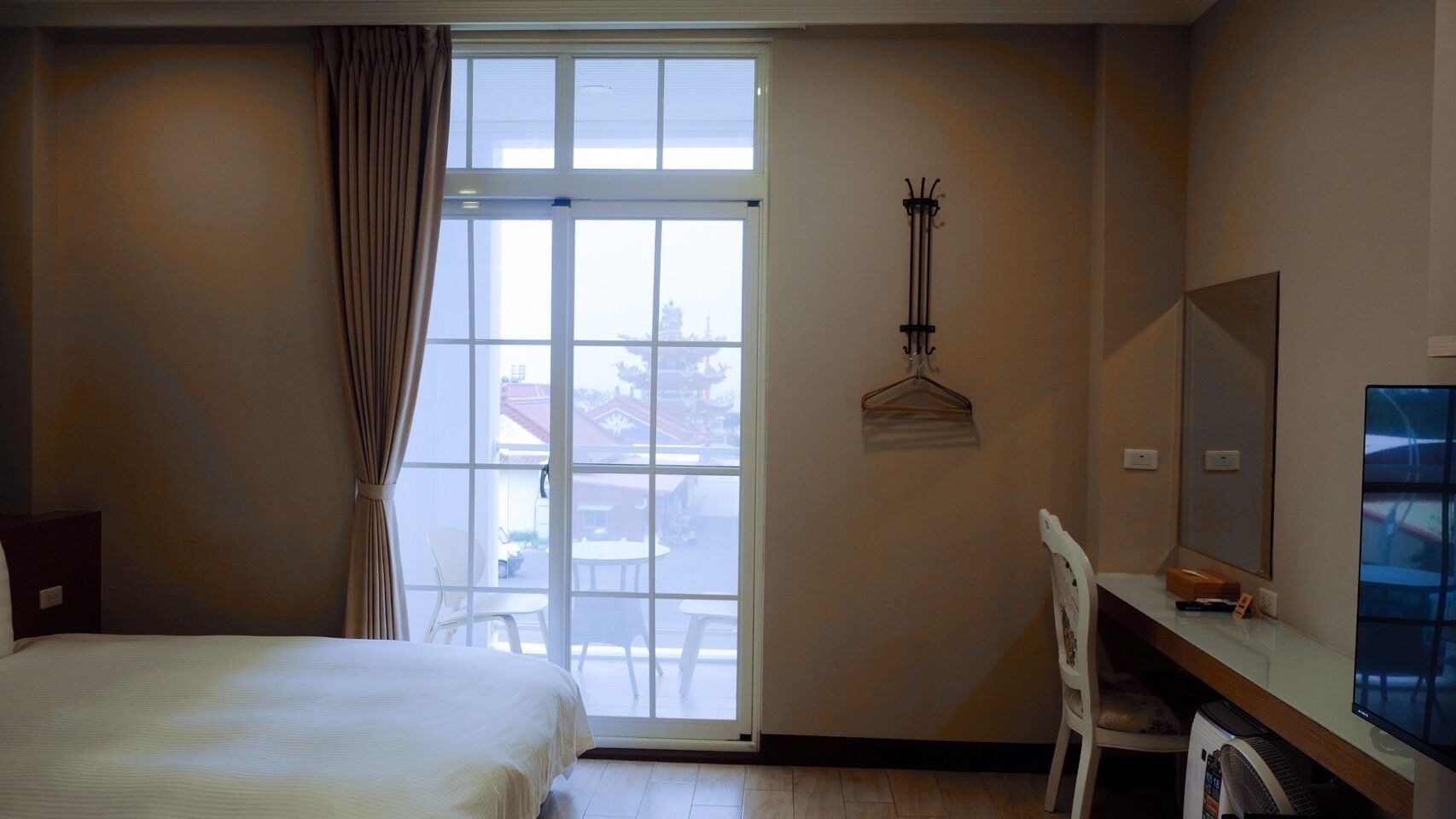 Hotelkamer met een bed, een bureau, een stoel, een kapstok en een groot raam met uitzicht.