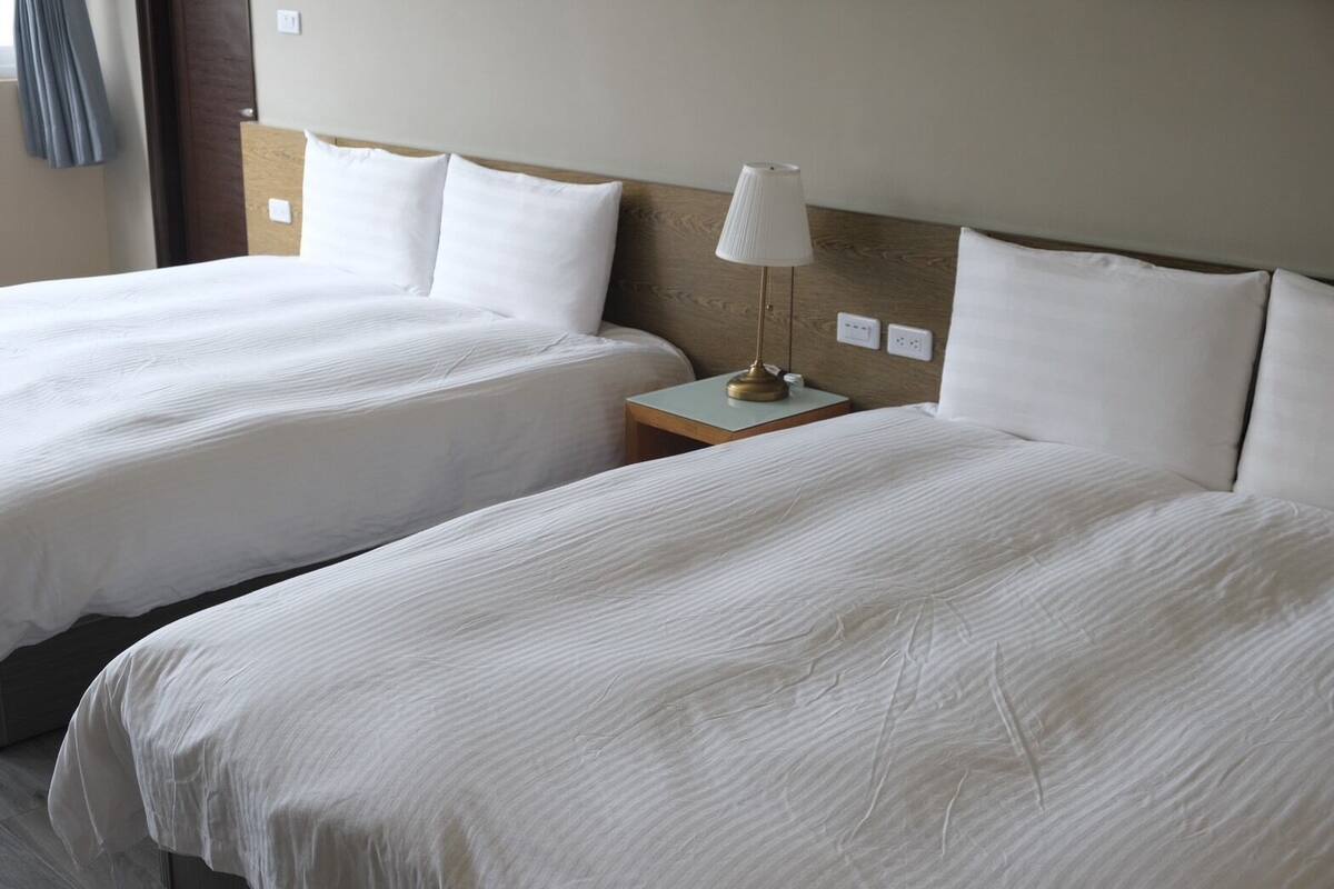 A hotel room with two single beds, a bedside table with a lamp, and a wooden headboard.
