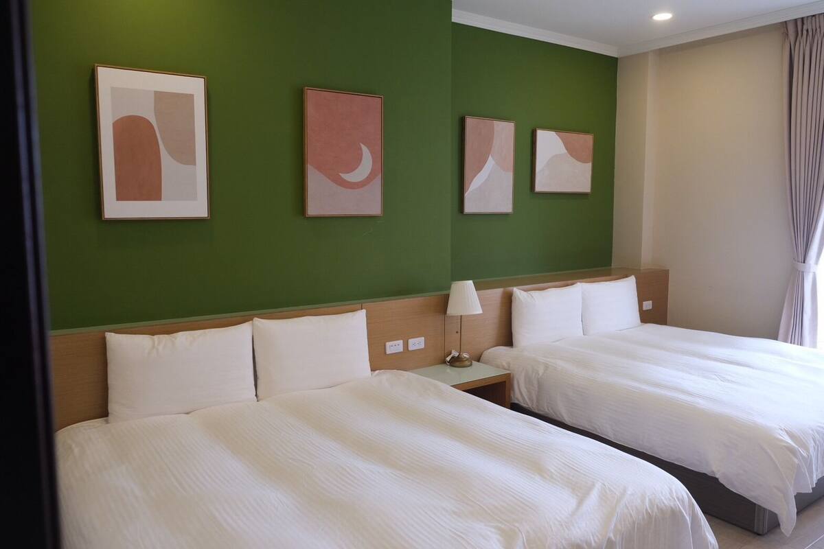 A hotel room with two beds, green walls, and abstract artwork.