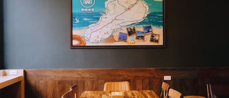 Interior de un restaurante con una mesa y sillas de madera, un mapa enmarcado en la pared y una pared de color oscuro.