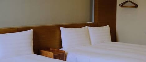 Habitación de hotel con dos camas, cabecero y mesita de noche de madera.