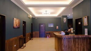 Zona de recepción de hotel con mostrador de madera, una puerta azul y una lámpara en el techo.