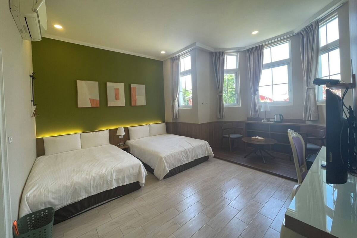 A hotel room with two beds, a desk, a chair, and a television.