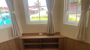 Un rincón con asientos que incluye un banco de madera y dos sillas, una mesita y una ventana con cortinas.