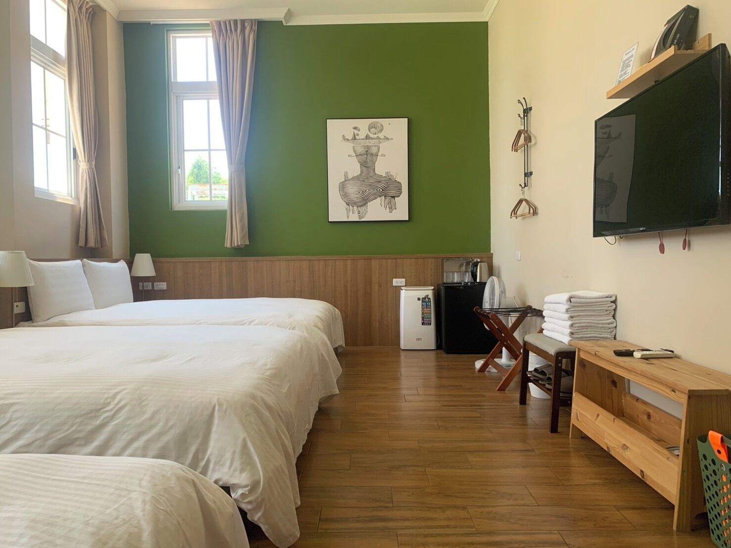 Habitación de hotel con dos camas, un escritorio con computadora, televisor y refrigerador pequeño.