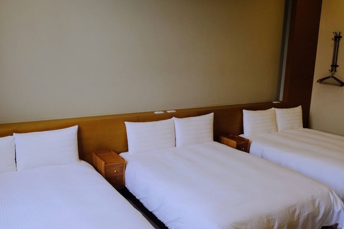 A hotel room with three single beds, wooden headboards, and a large mirror above the beds.