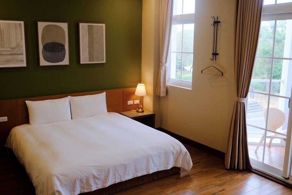 A hotel room with a bed, a nightstand with a lamp, and three framed artworks on the wall.