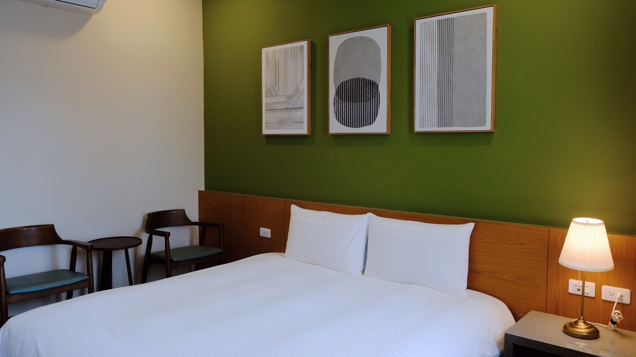 Habitación de hotel con cama, dos sillas, una mesa y tres cuadros enmarcados en la pared.