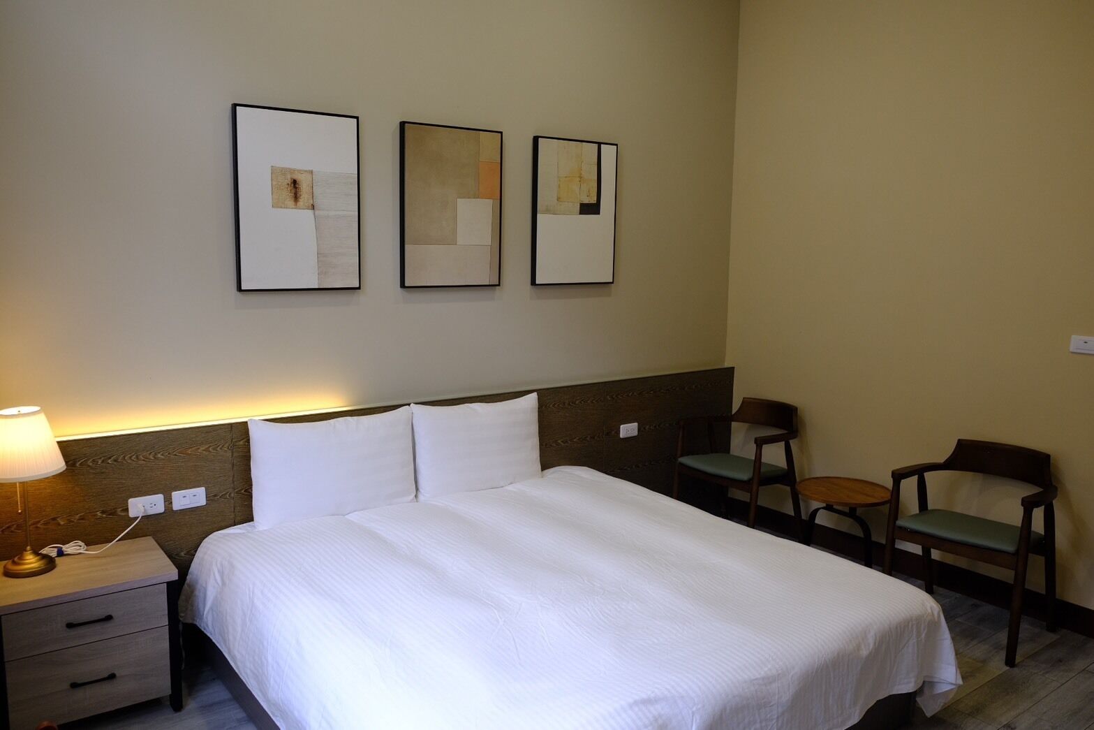 A hotel room with a bed, two chairs, a small table, and a lamp.