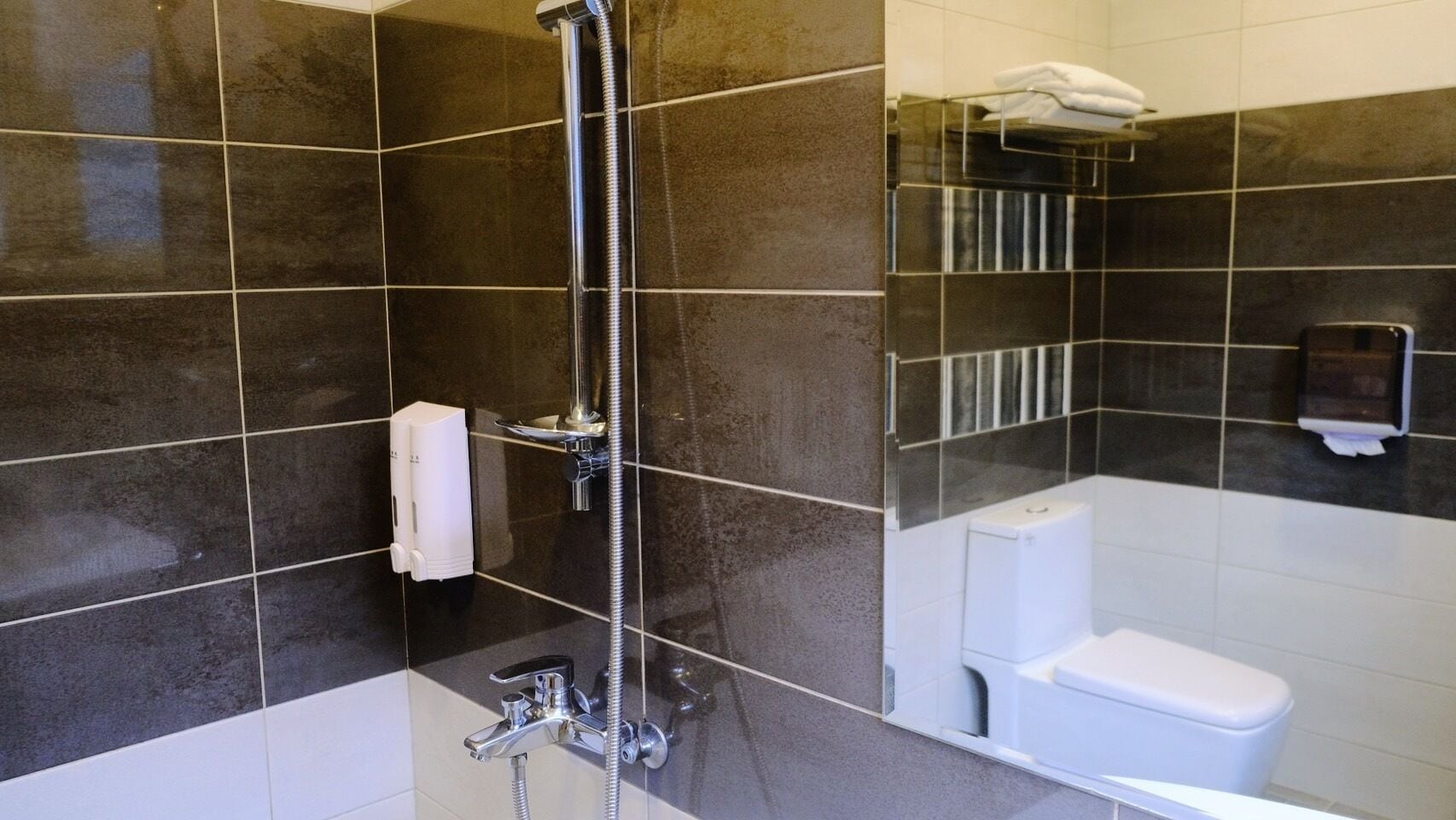 A modern bathroom with dark tiles, a shower, a toilet, and a towel rack.