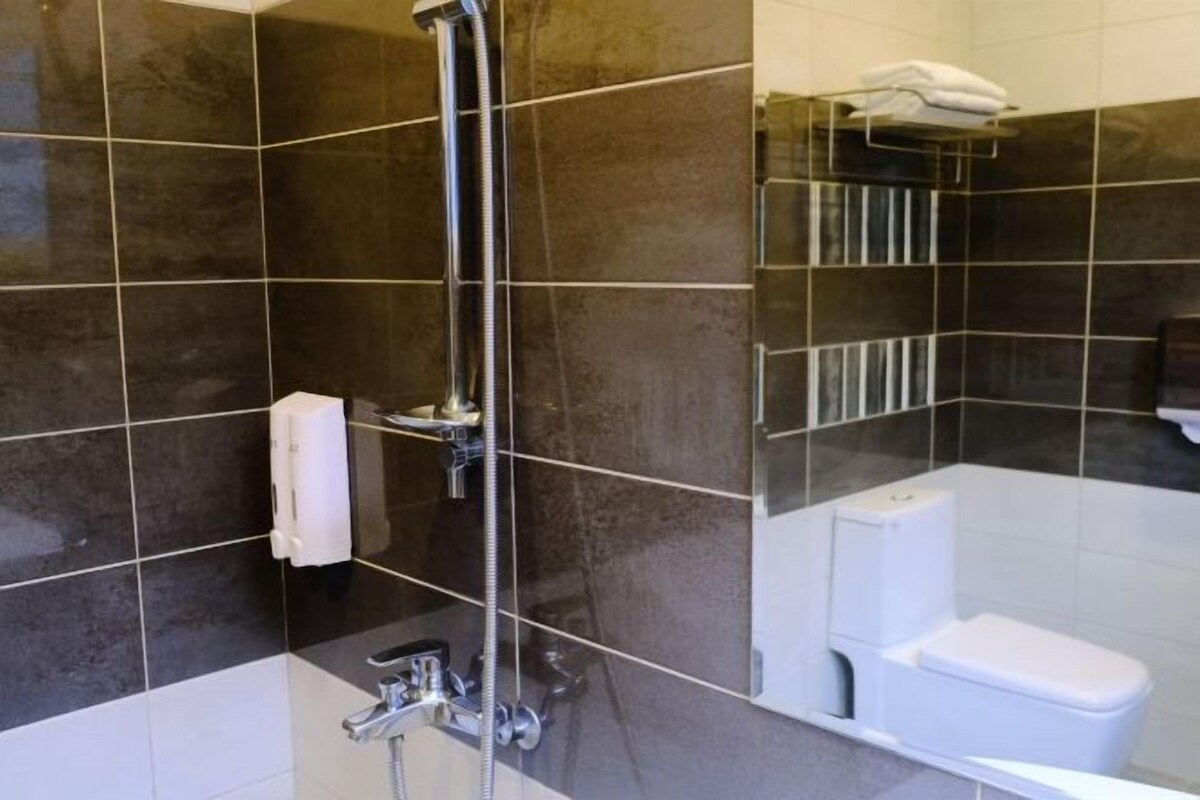 Un baño moderno con baldosas oscuras, ducha, inodoro y toallero.