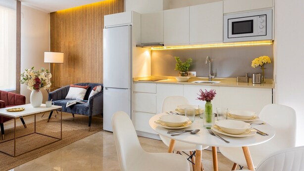 Une cuisine moderne avec des meubles blancs, un micro-ondes encastré et un coin repas doté d’une table blanche, mise pour quatre personnes.