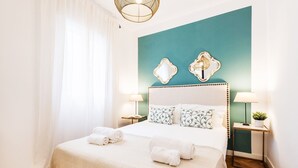 A neatly made bed with white linens and two pillows, a teal accent wall, and two wall-mounted mirrors.
