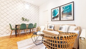 A modern living room with a sofa, green chairs, a wicker chair, and two framed artworks on the wall.