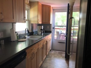 A kitchen with wooden cabinets, a stainless steel sink, a coffee maker, and a view through a glass door to an outdoor deck.