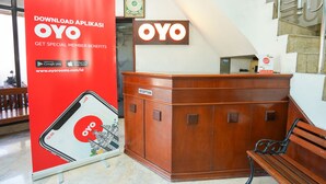 Ein Empfangsbereich mit einem Holztresen, einem roten Banner, der die OYO App bewirbt, und einer Treppe im Hintergrund.