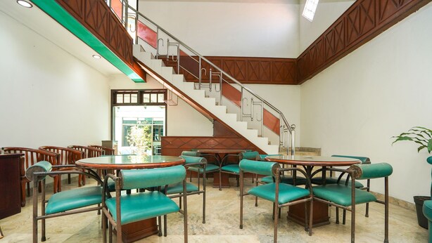 Eine geräumige Lobby mit einer zentralen Treppe, mehreren Sitzbereichen mit grünen Polsterstühlen und einem Marmorboden.