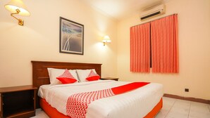 Ein Hotelzimmer mit einem großen Bett, einem Nachttisch, einer Wandleuchte, einer Klimaanlage und einem Fenster mit Vorhängen.