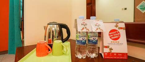 A table with a tray holding two mugs, a kettle, and two bottles of water. There is a carton of OYO branded water and a sign asking for a review.