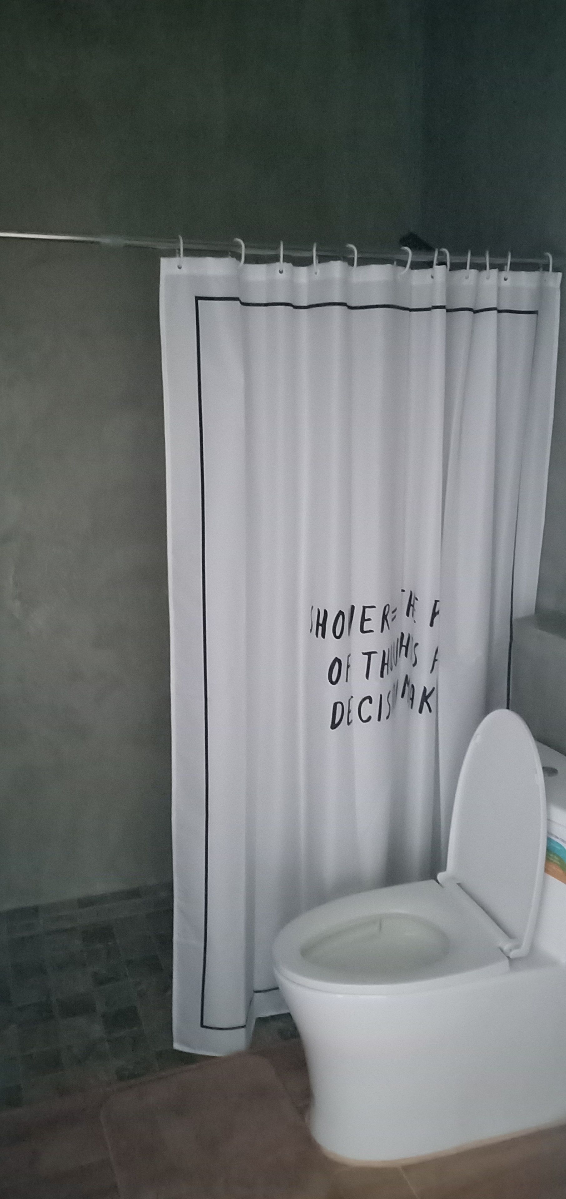 A bathroom with a white toilet, a white shower curtain with black text, and a tiled floor.
