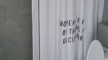 A bathroom with a white toilet, a white shower curtain with black text, and a tiled floor.